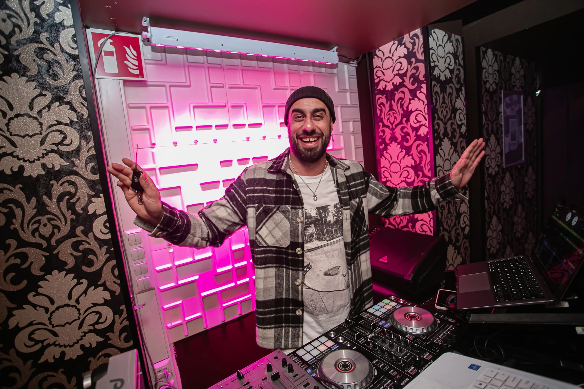 DJ Snabu hymyilemässä kädet levitettyinä DJ-pöydän takana